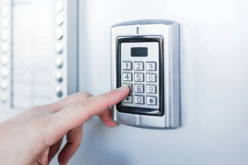 Une personne utilise un digicode d'accès sécurisé installé sur une porte d'entrée, appuyant sur le clavier numérique pour saisir un code