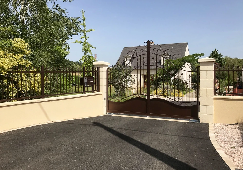 Portail d'entrée double battant en fer forgé brun, style classique ornemental avec volutes et flèches décoratives, monté sur piliers en pierre calcaire