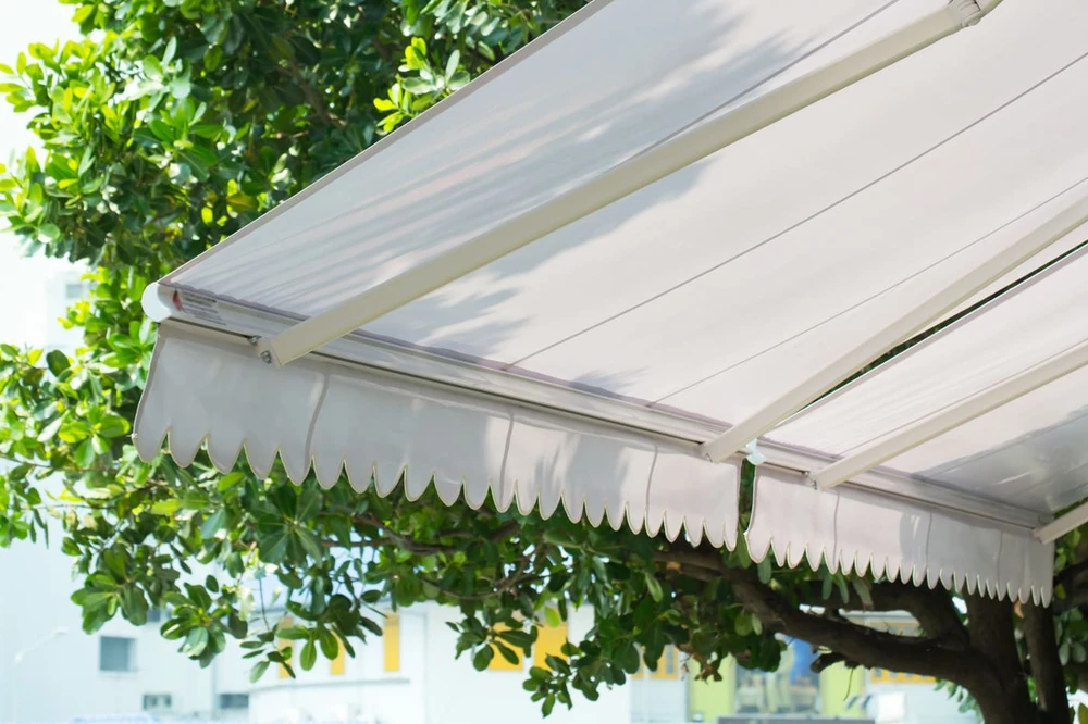 Store banne rétractable blanc crème, vue en contre-plongée, déployée en extérieur