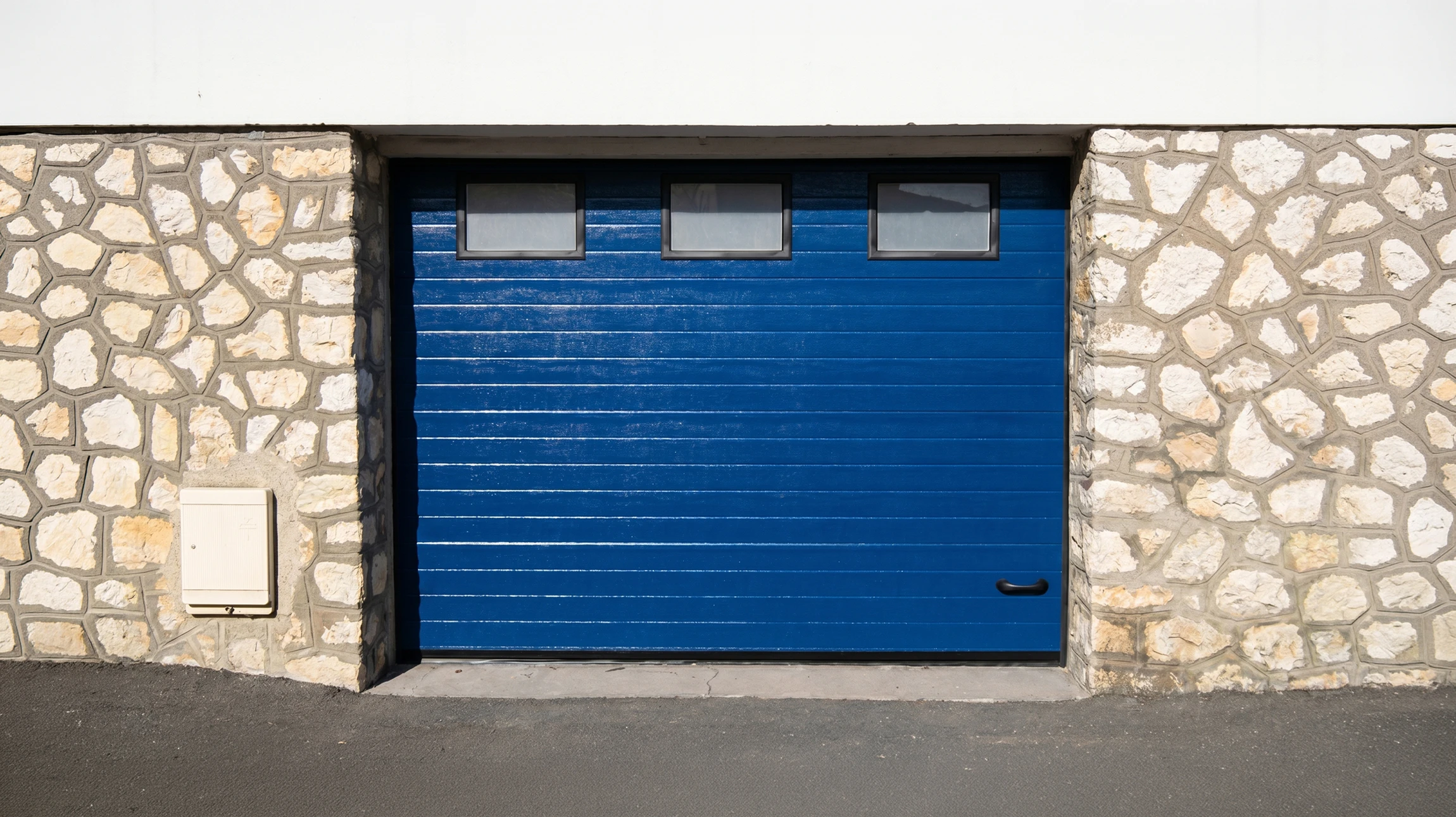 Façade extérieure résidentielle avec porte de garage sectionnelle grise à panneaux horizontaux lisses intégrée dans mur en pierre naturelle beige-rosé